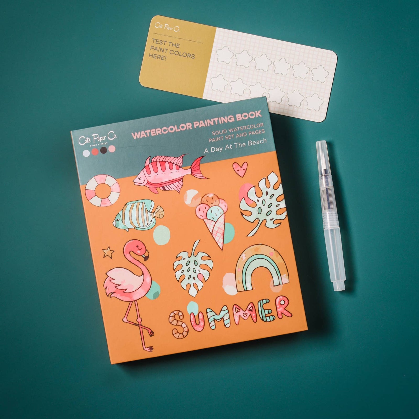 Watercolor painting book titled 'A Day at the Beach' with a pen on a teal background