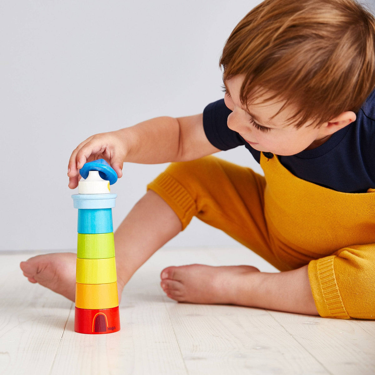 Child playing with a colorful stack of blocks on a light wooden floor.