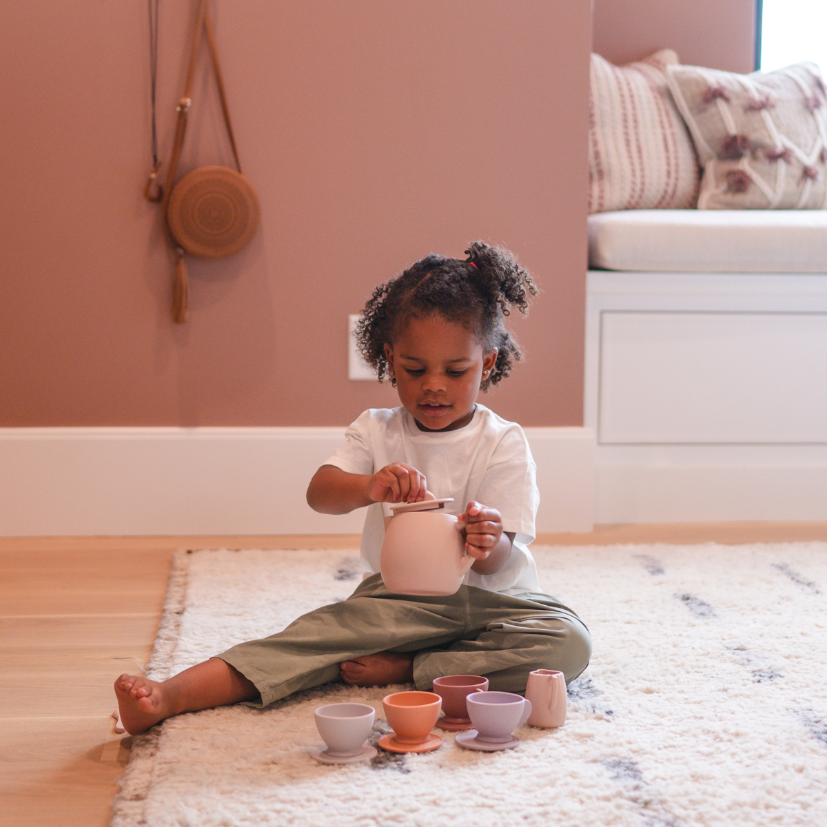 Child playing with colorful silicone pot on a rug in a room.