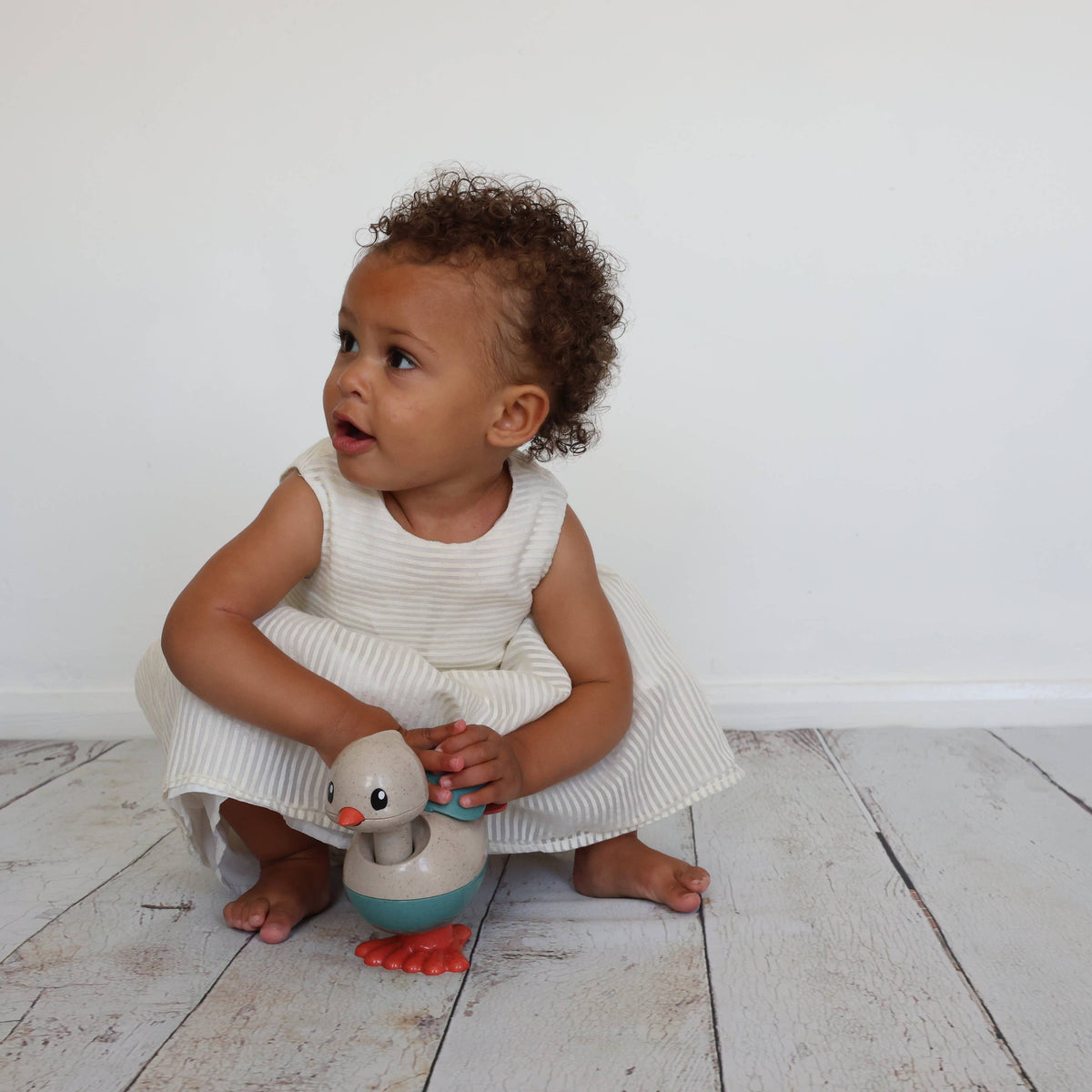 Child holding a toy duck on a white wooden floor