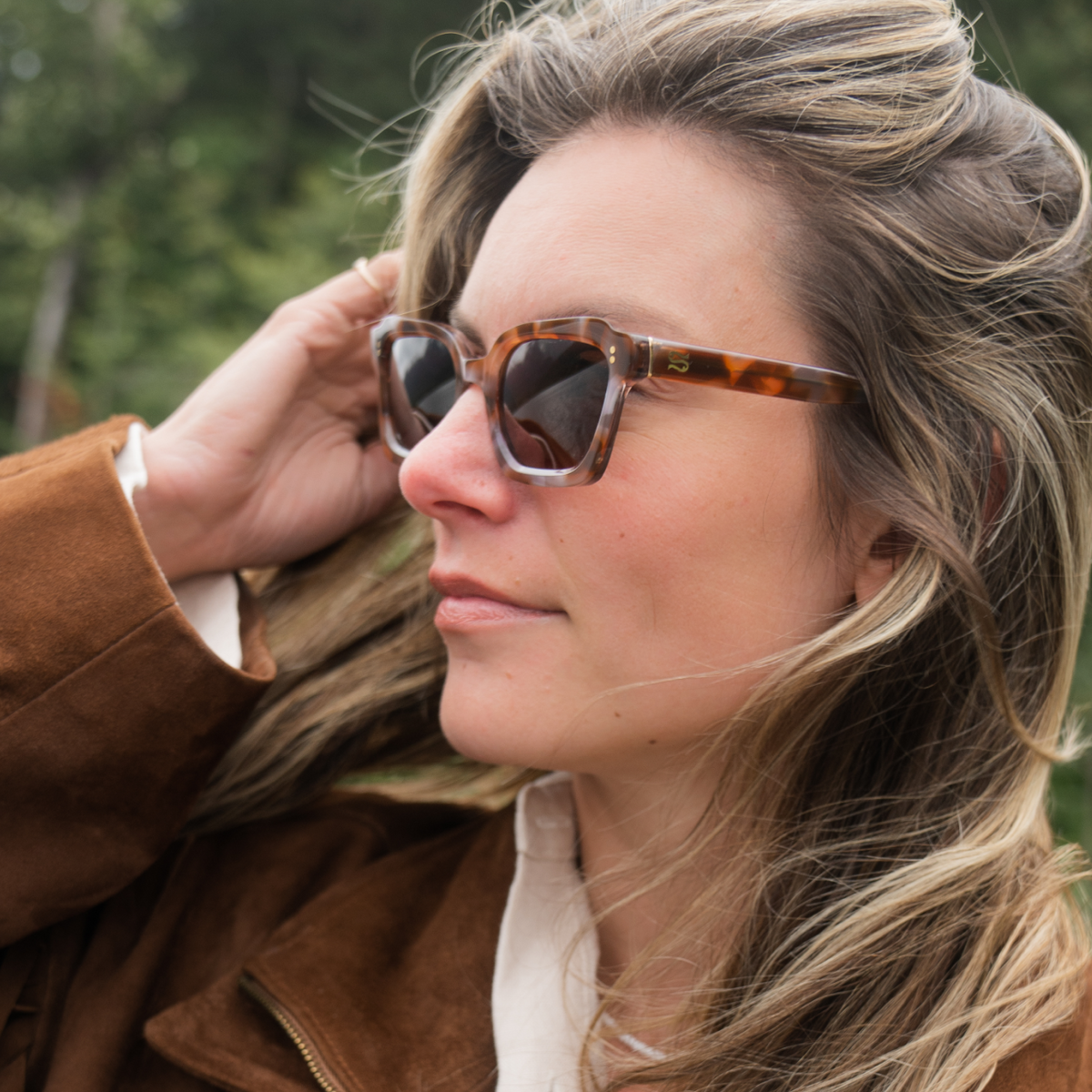 Woman wearing tortoiseshell sunglasses and a brown coat outdoors