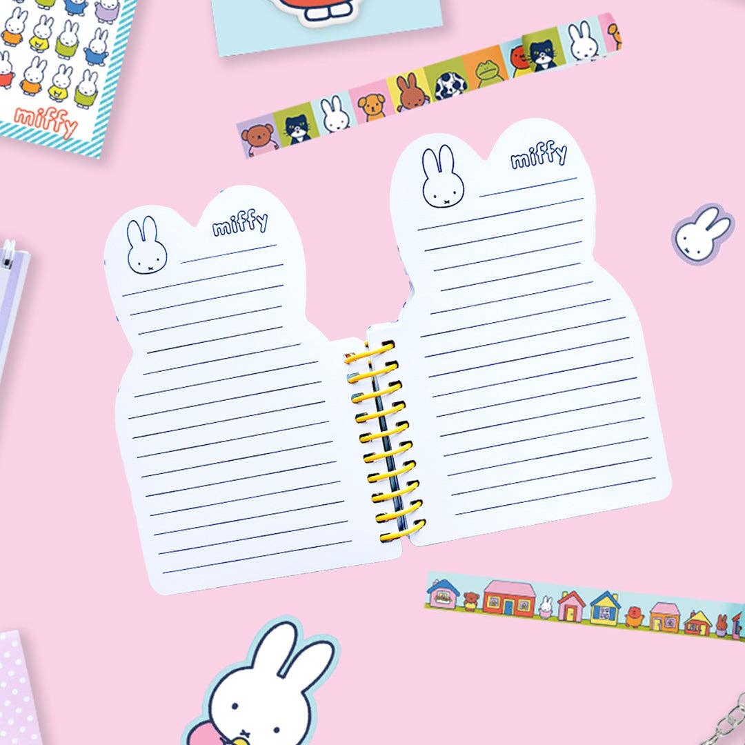A cute Miffy-themed split notepad with bunny illustrations and lined writing pages, displayed on a pink background with other stationery items.