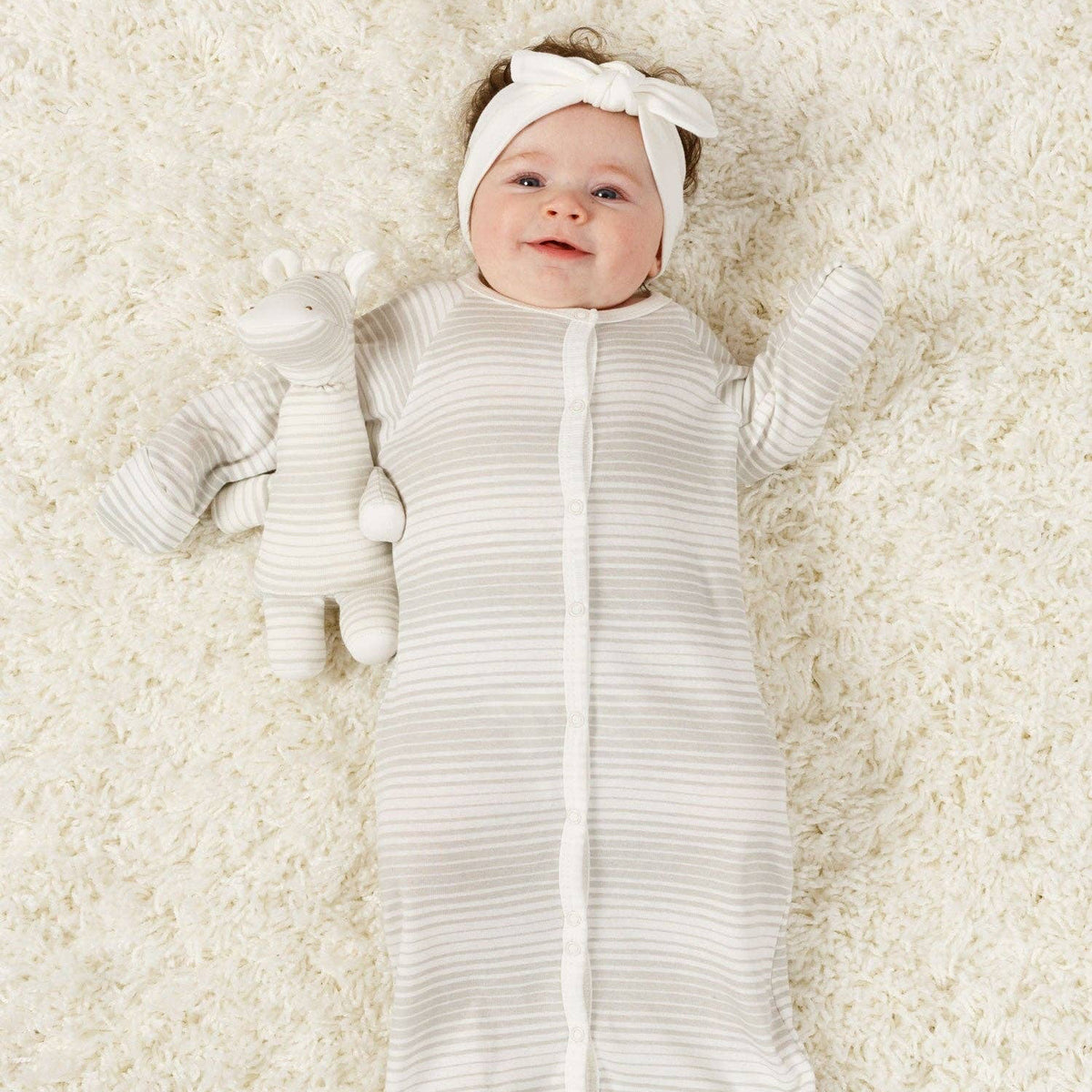 Baby in a white swaddle and headband lying on a soft, light-colored surface