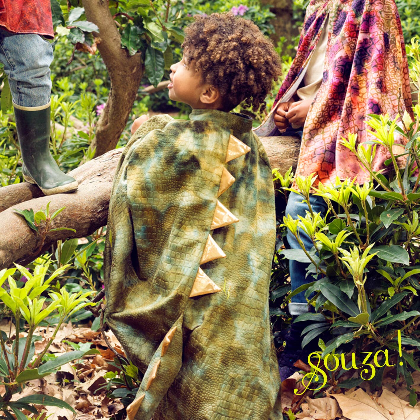 Child in a green dinosaur costume standing in a forest