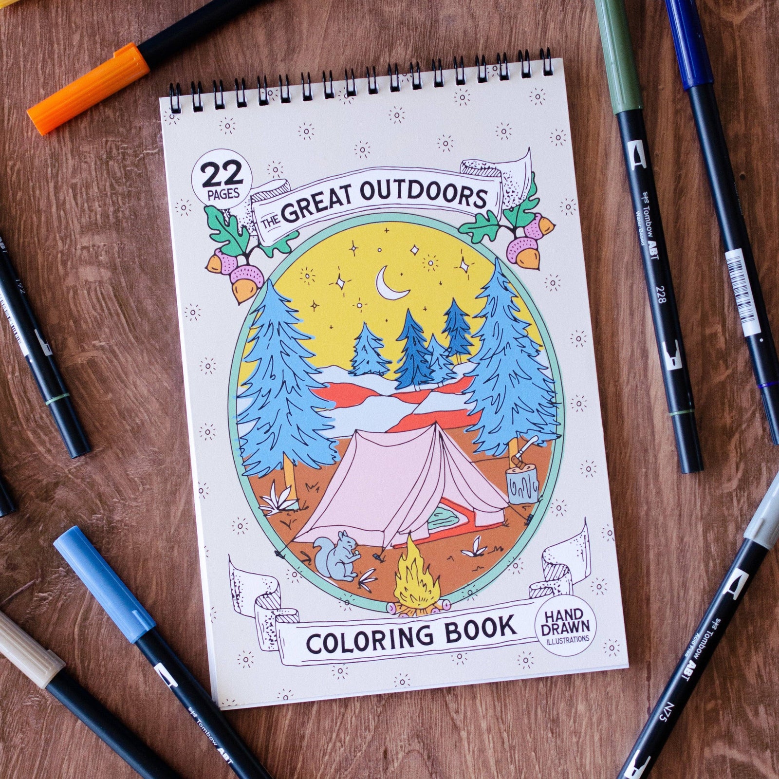 Coloring book titled 'The Great Outdoors' on a wooden surface with markers around it.