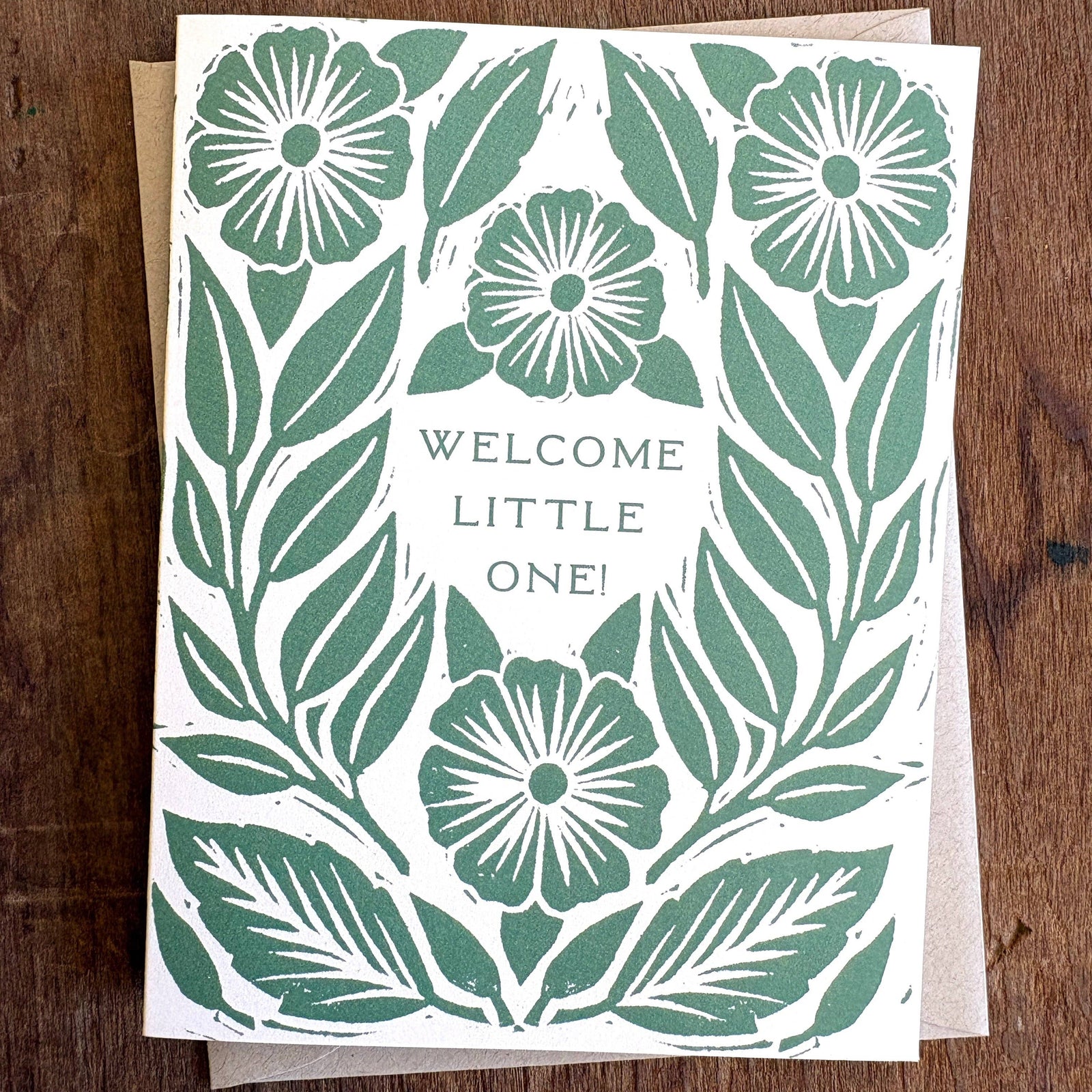Greeting card with floral design and 'Welcome Little One!' text on a wooden surface