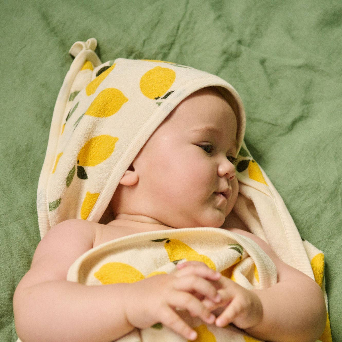 Baby wrapped in a yellow and white towel with lemon pattern on a green background