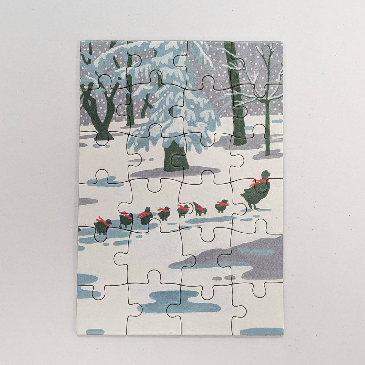 A completed jigsaw puzzle featuring a winter forest scene with snow-covered trees, blue-gray ground, and a goose pulling a sled with red accents, photographed against a plain light background.