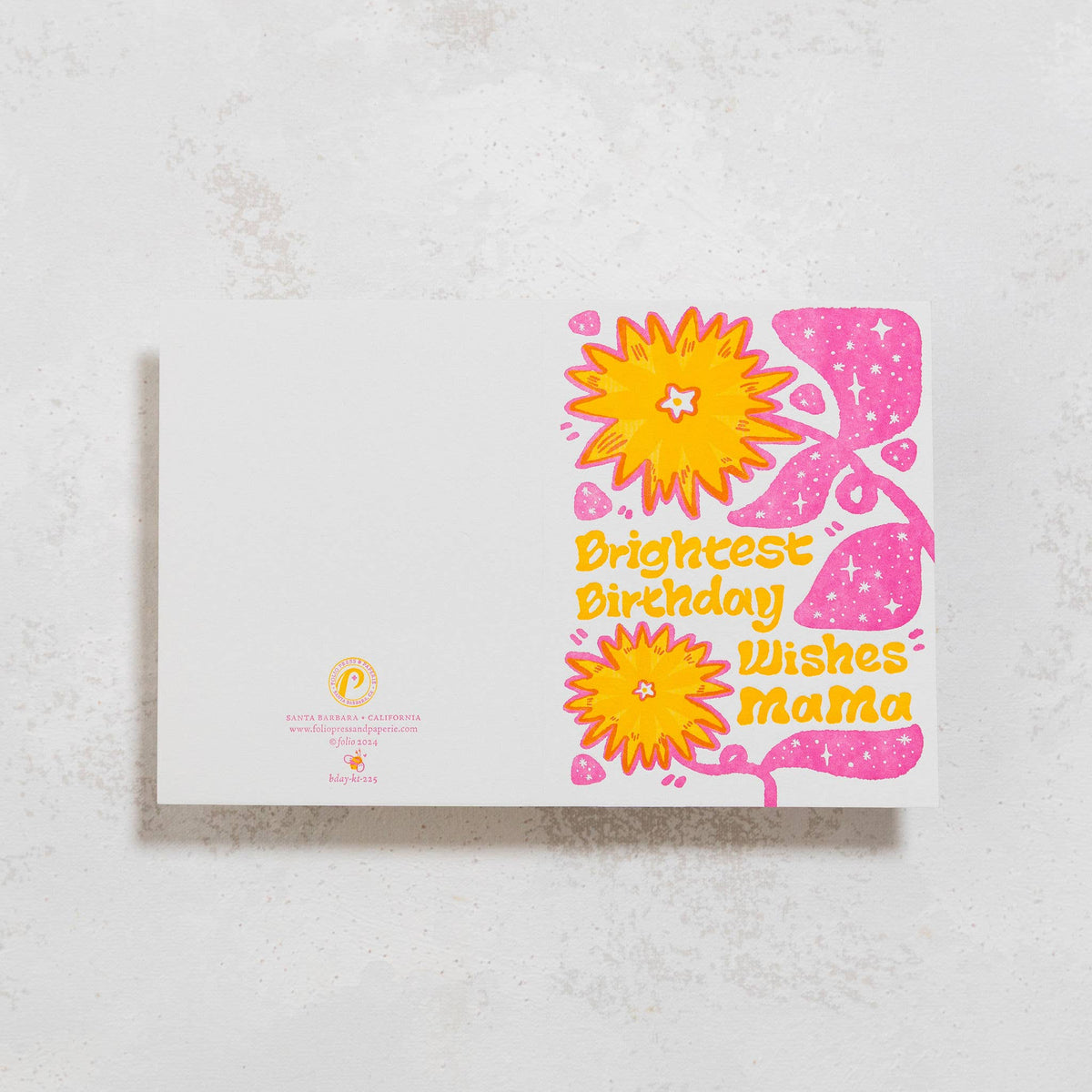 A rectangular greeting card with a white background and a colorful floral design on the right side, reading 'Brightest Birthday Wishes Mama' in yellow text. The card is photographed from above on a light textured surface.