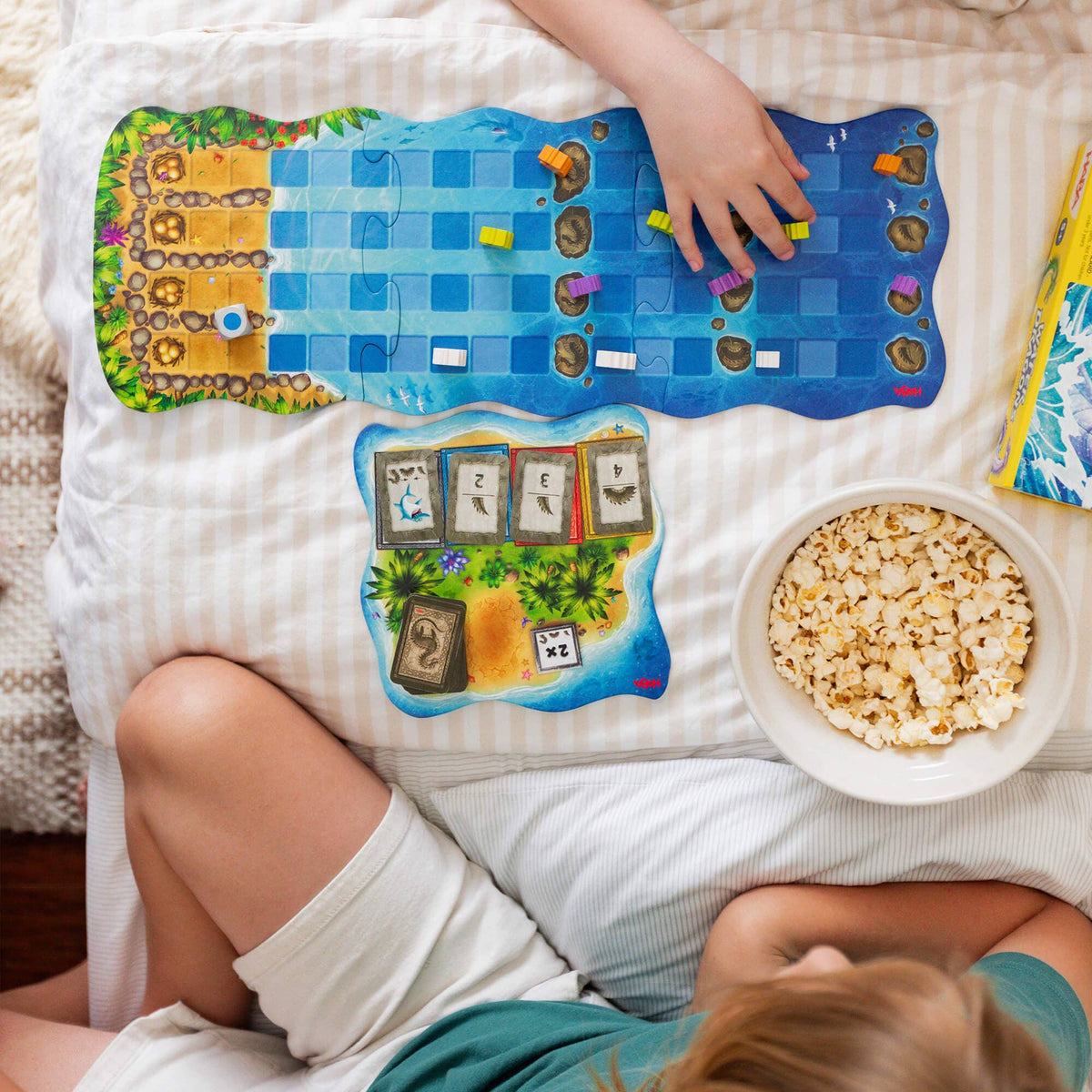 Child playing a board game with a bowl of popcorn on a bed