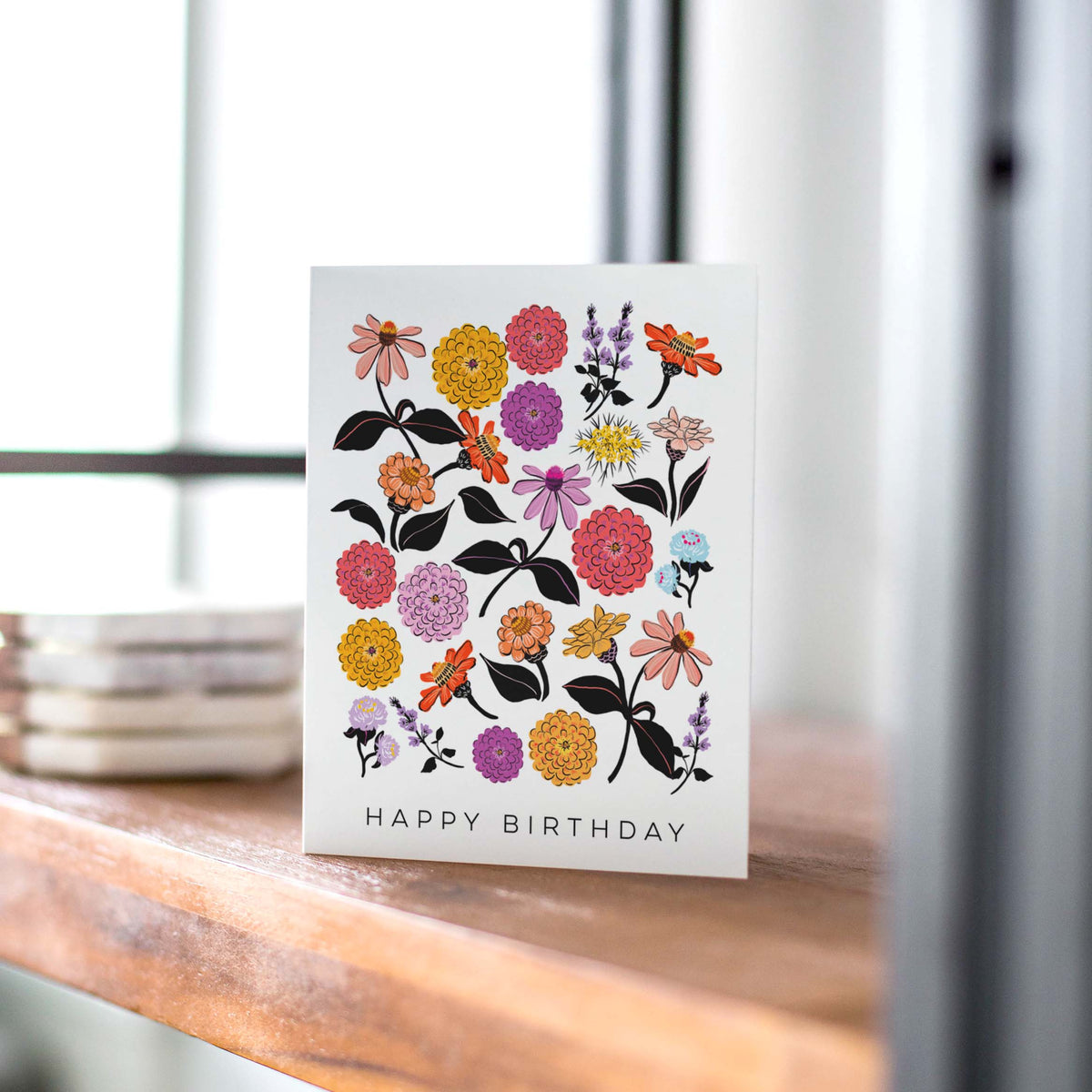 Greeting card with floral design and &#39;Happy Birthday&#39; text on a wooden surface.