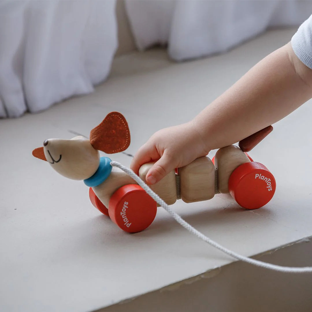 Child pulling a wooden toy with wheels on a light surface