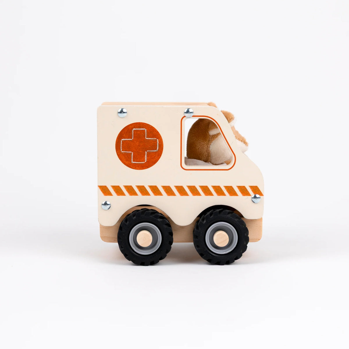 A wooden toy ambulance with a cream-colored body, orange accents including a cross symbol and hazard stripes, black wheels, and a plush animal inside the driver's seat, shown on a white background.