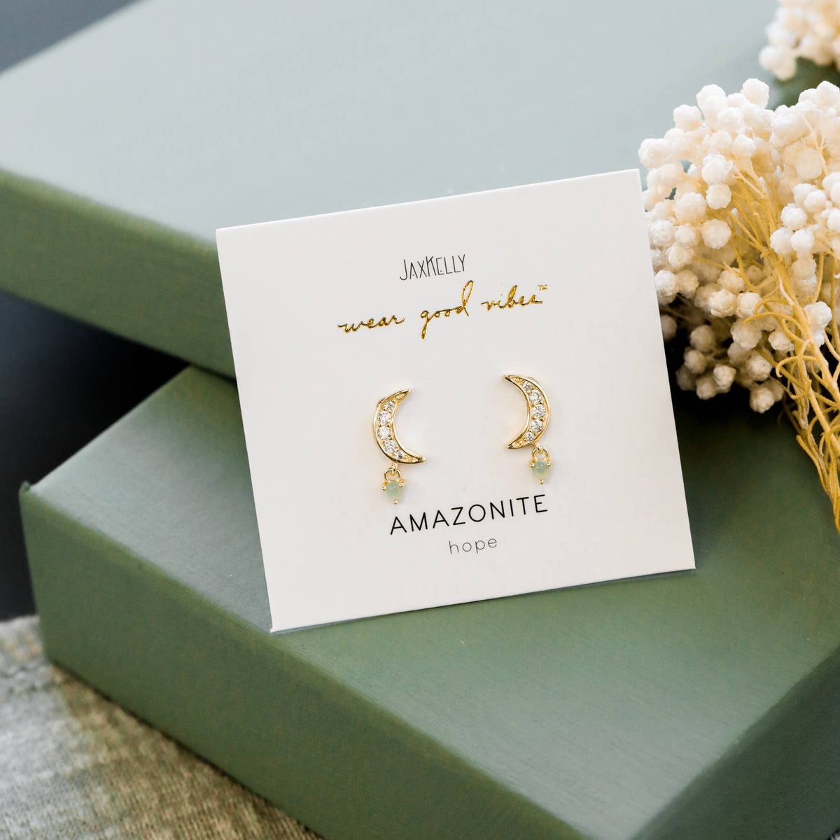 Gold earrings on a card with 'Amazonite' text, displayed on a green box.