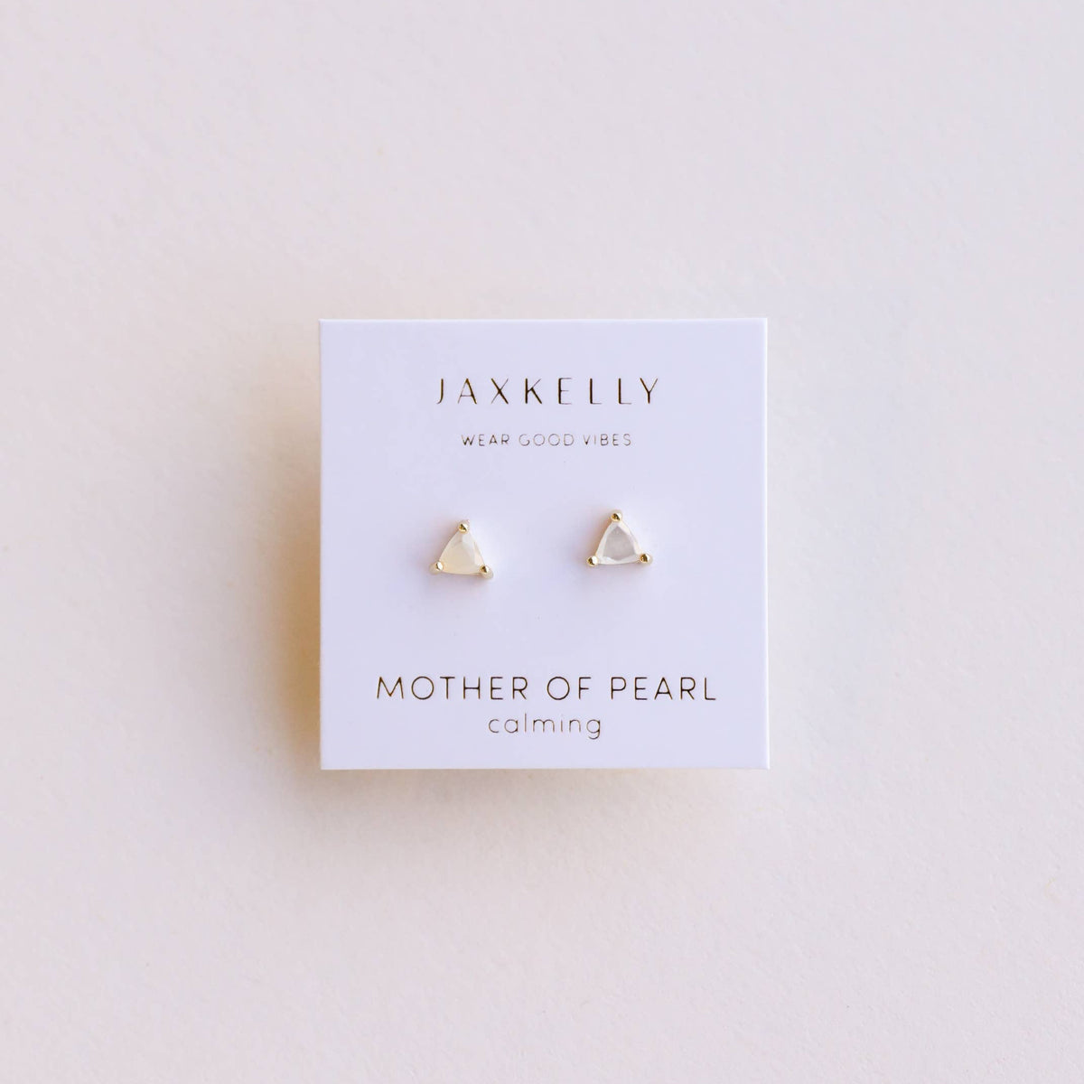 Pair of gold triangular earrings on a Jax Kelley branded card with 'Mother of Pearl' and 'Calming' text on a light background.