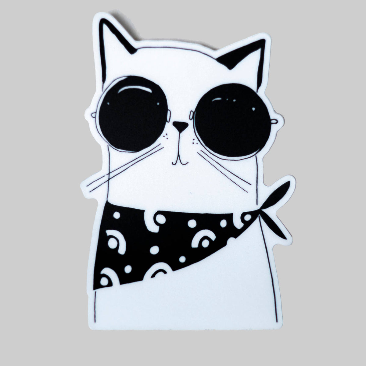 A die-cut sticker featuring a cartoon cat wearing black round sunglasses and a black bandana with white dots, shown on a solid light gray background.