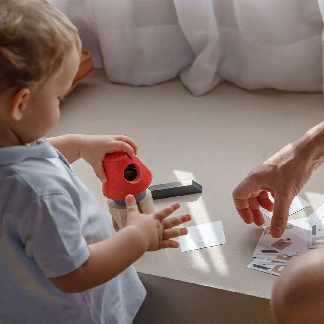 Child playing with a toy and an adult's hand on a light-colored surface.