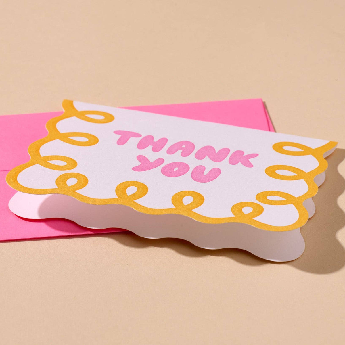 Card with 'Thank you' on a pink envelope against a beige background