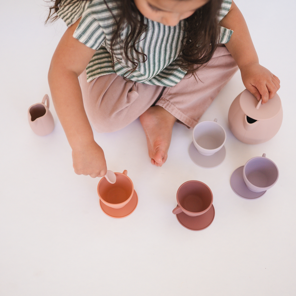 Child playing with colorful silicone cups and pots on a white surface