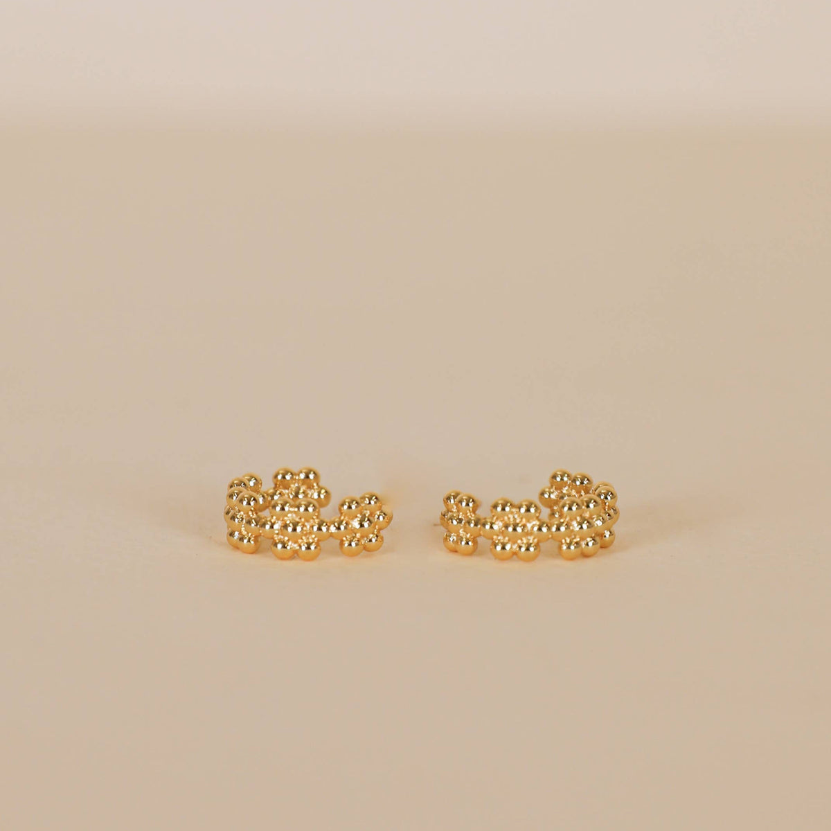 Gold chain-style earrings on a beige background