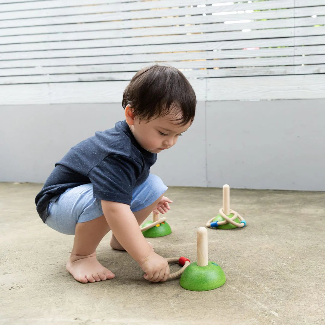 Child playing with green wooden toys on a concrete floor.