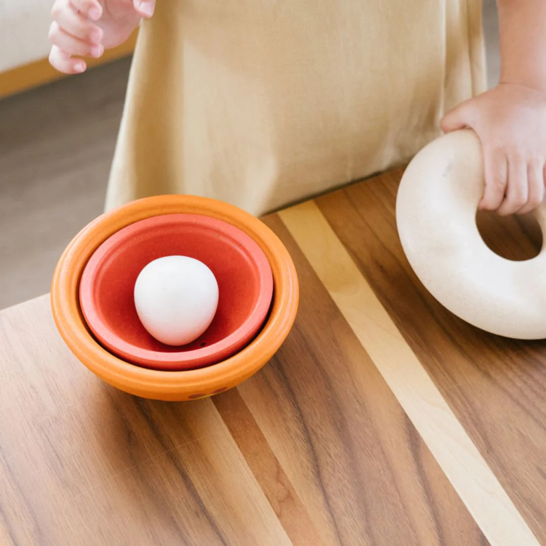 Orange and red bowl with a white ball on a wooden surface, with a person's legs in the background.