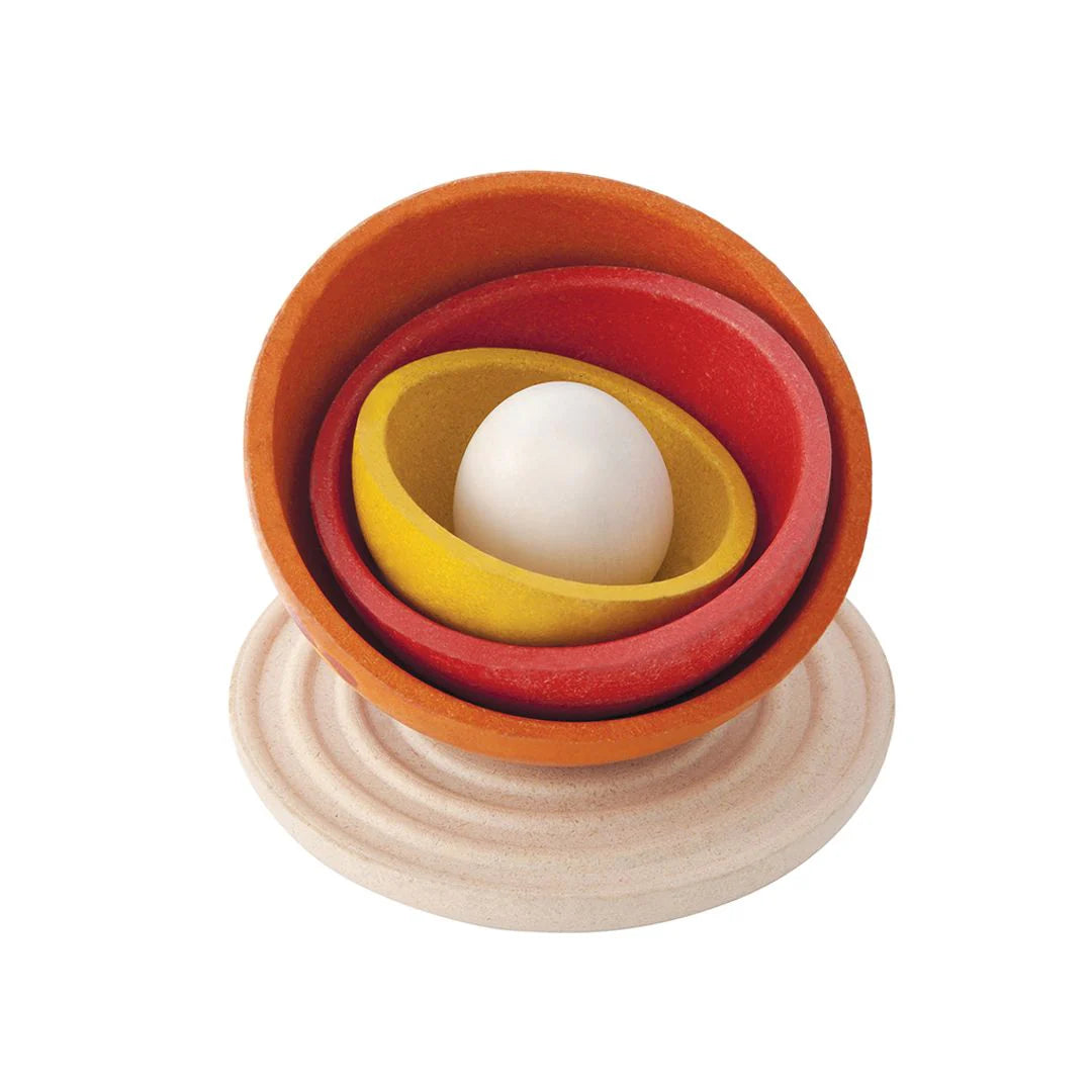 Set of wooden nesting bowls with a white egg inside on a white background
