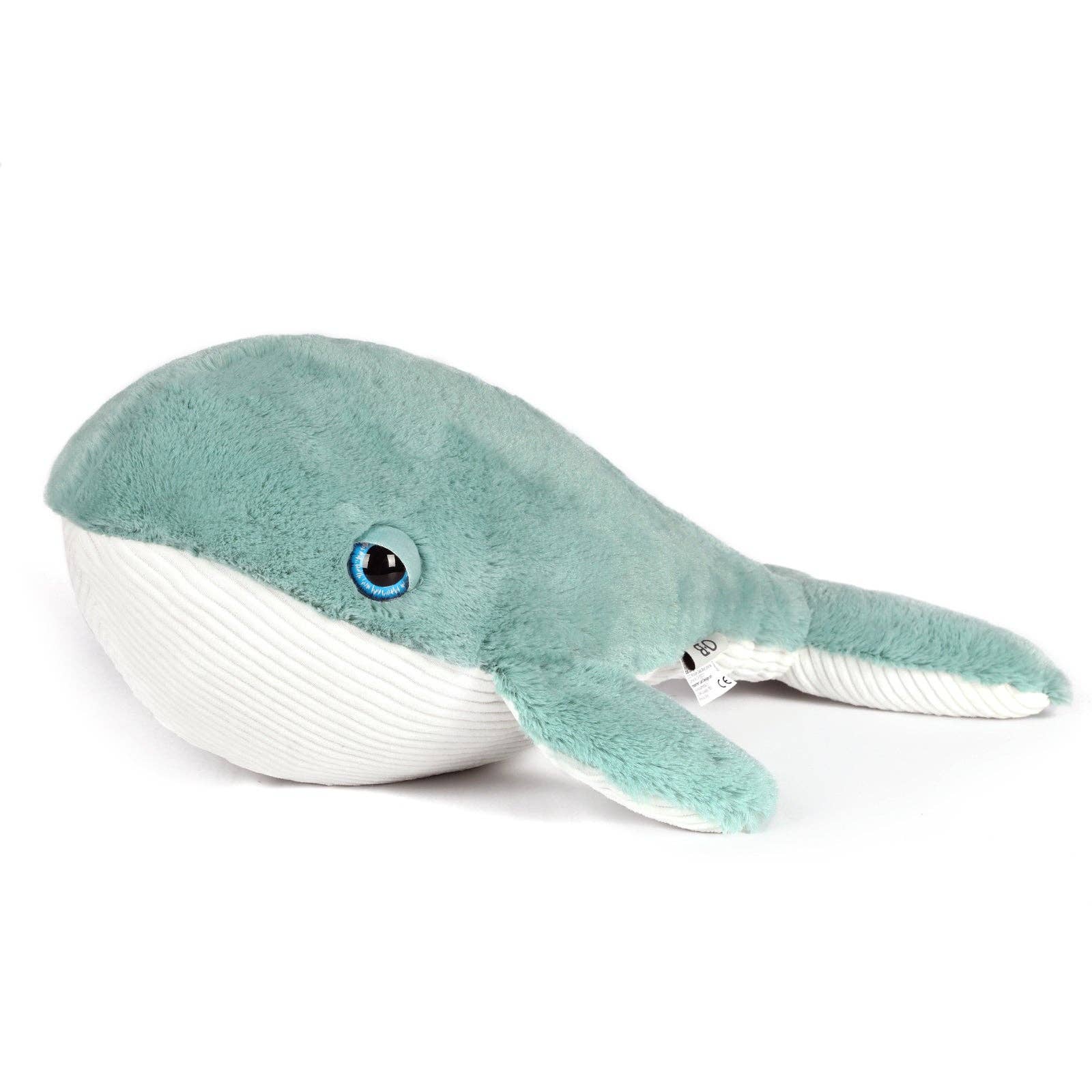 Plush whale toy held by a person on a beach with ocean in the background