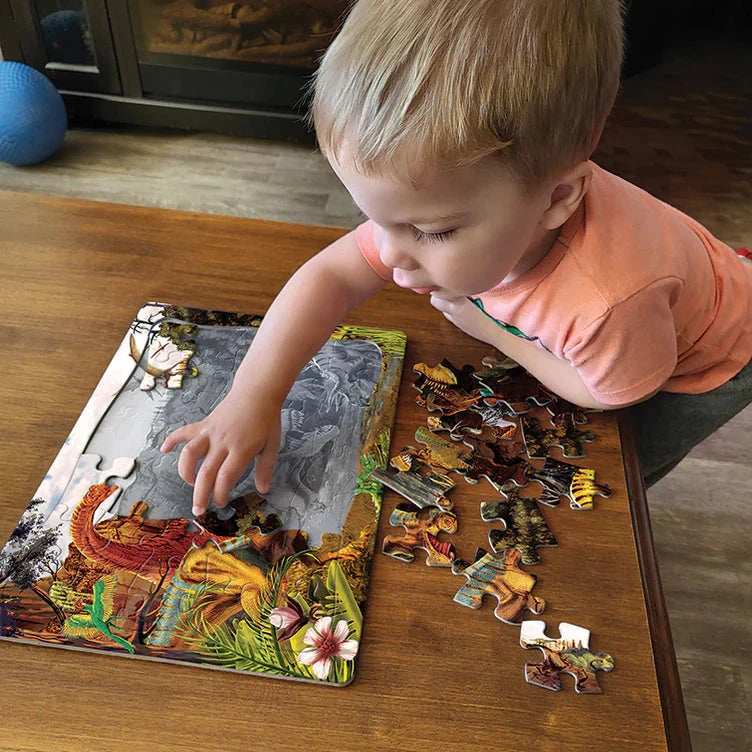 Child playing with a dinosaur puzzle on a wooden table.