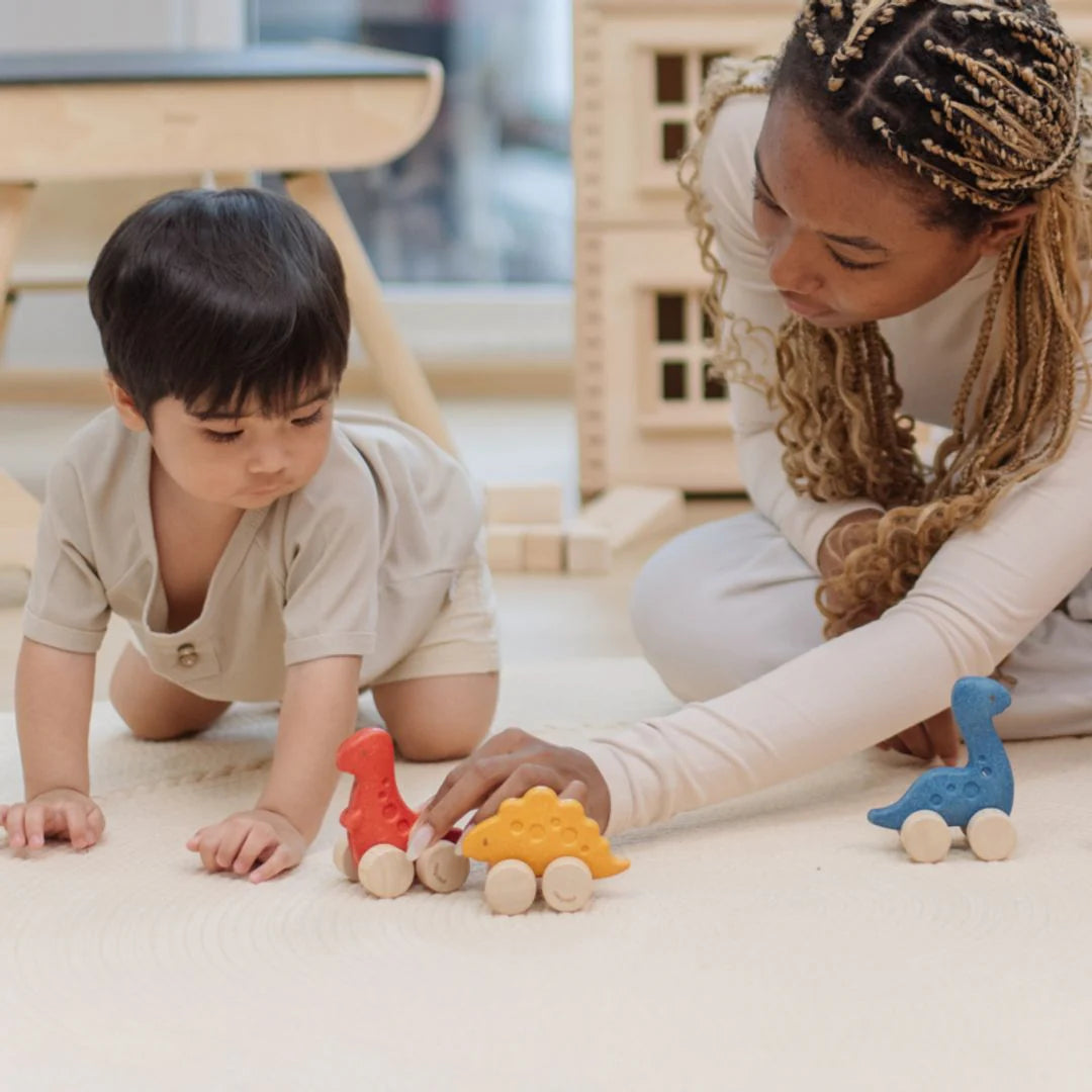 Two people playing with colorful wooden toys on a light-colored floor.