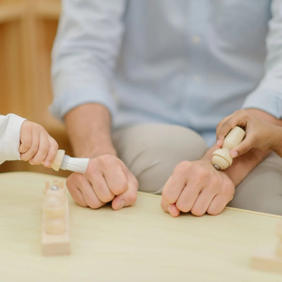 Two people playing with wooden toys on a light surface.