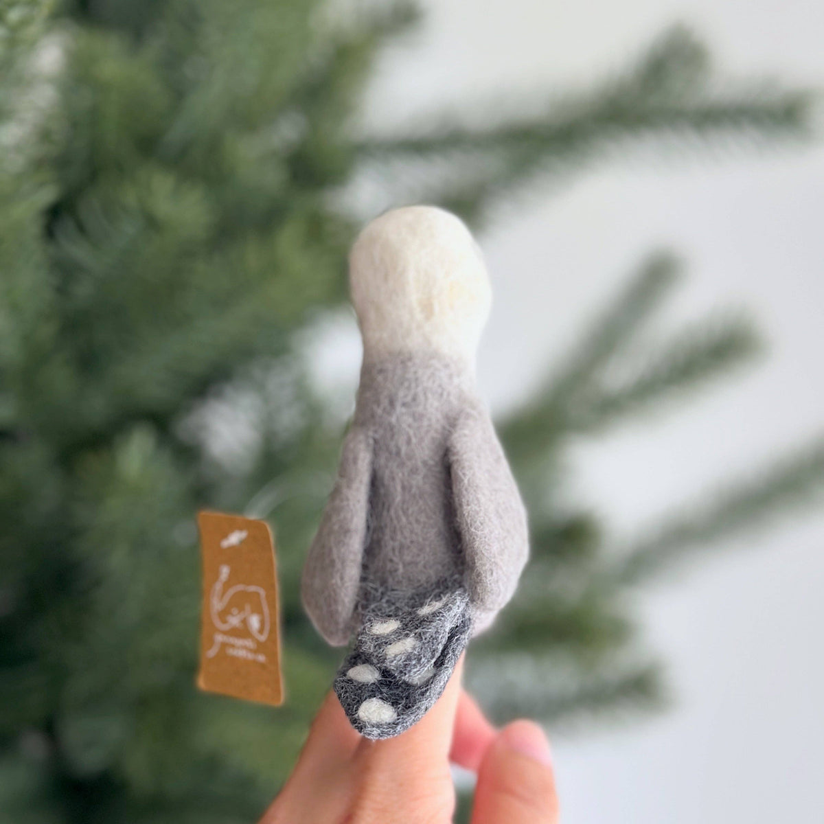 Small felted animal toy held between fingers with a blurred green background