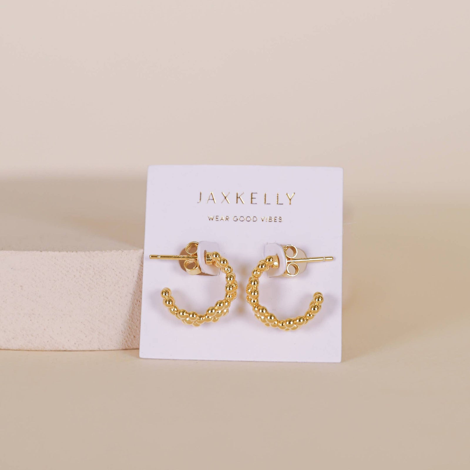 Gold hoop earrings on a Jax Kelly branded card against a beige background