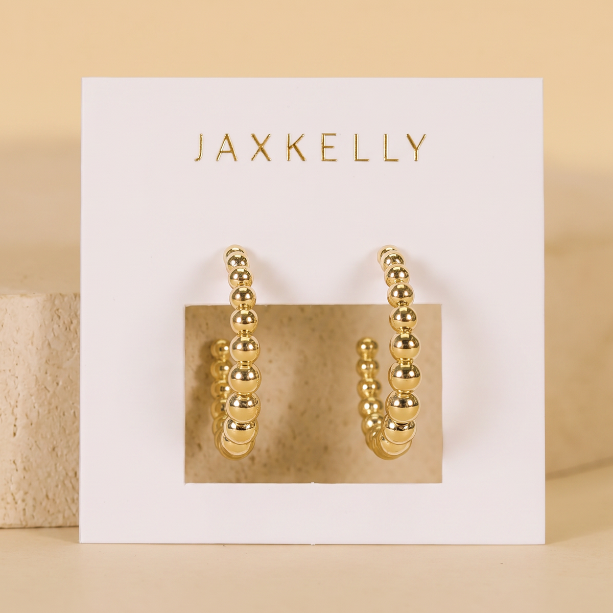Gold hoop earrings on a Jaxkelly branded card with a beige background