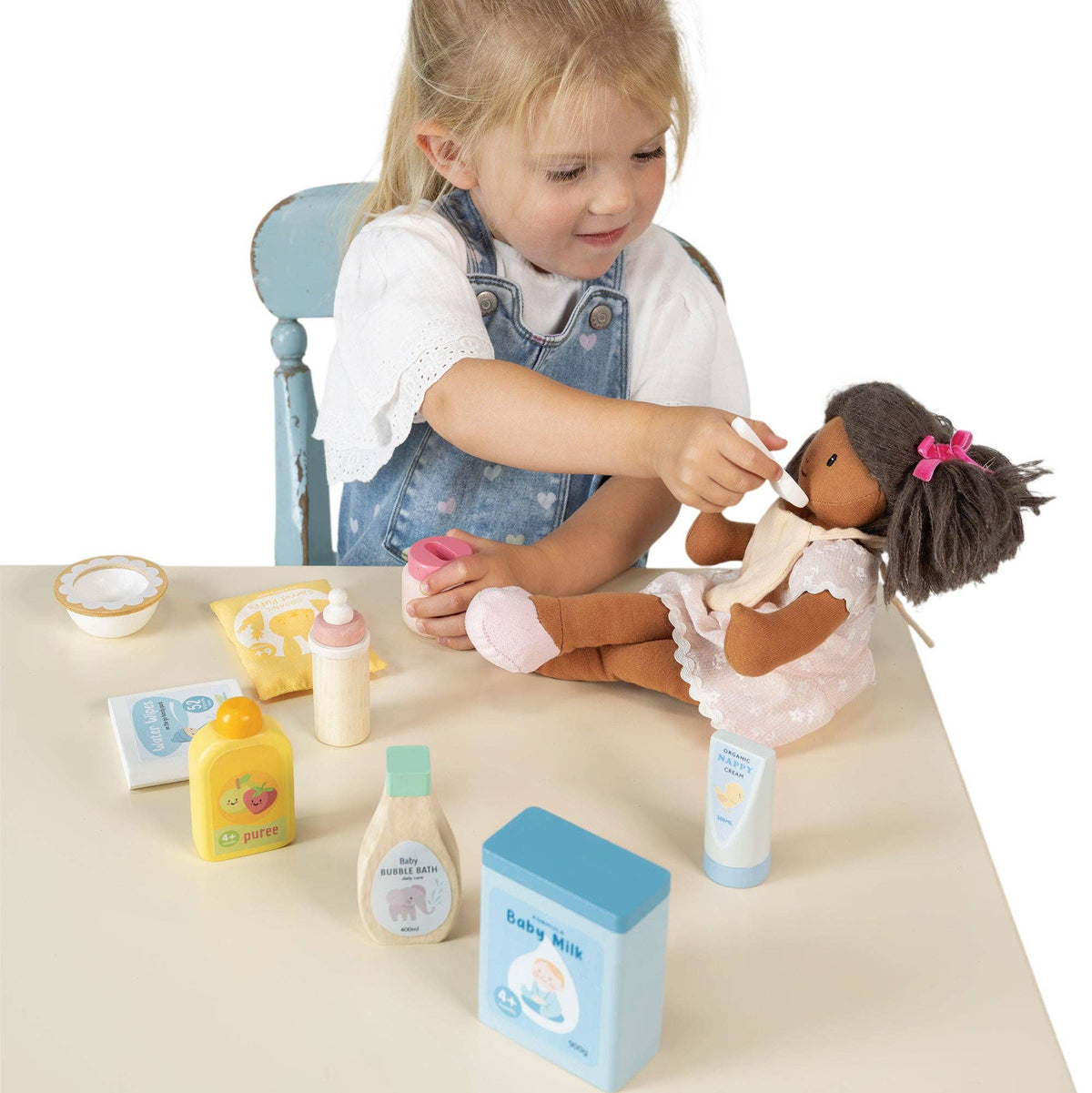 Child playing with a doll and toy bathroom set on a table.