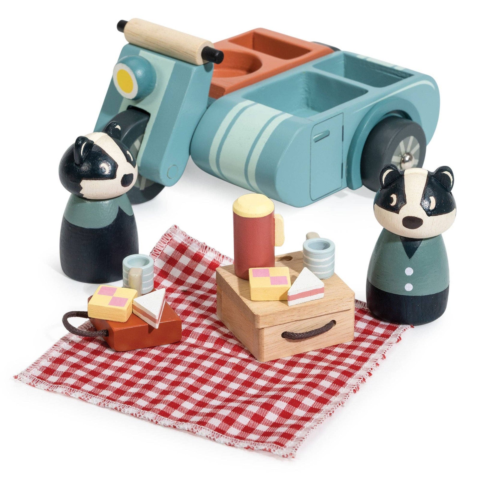 Wooden toy set with a scooter, picnic basket, and two badger figures on a red checkered cloth.