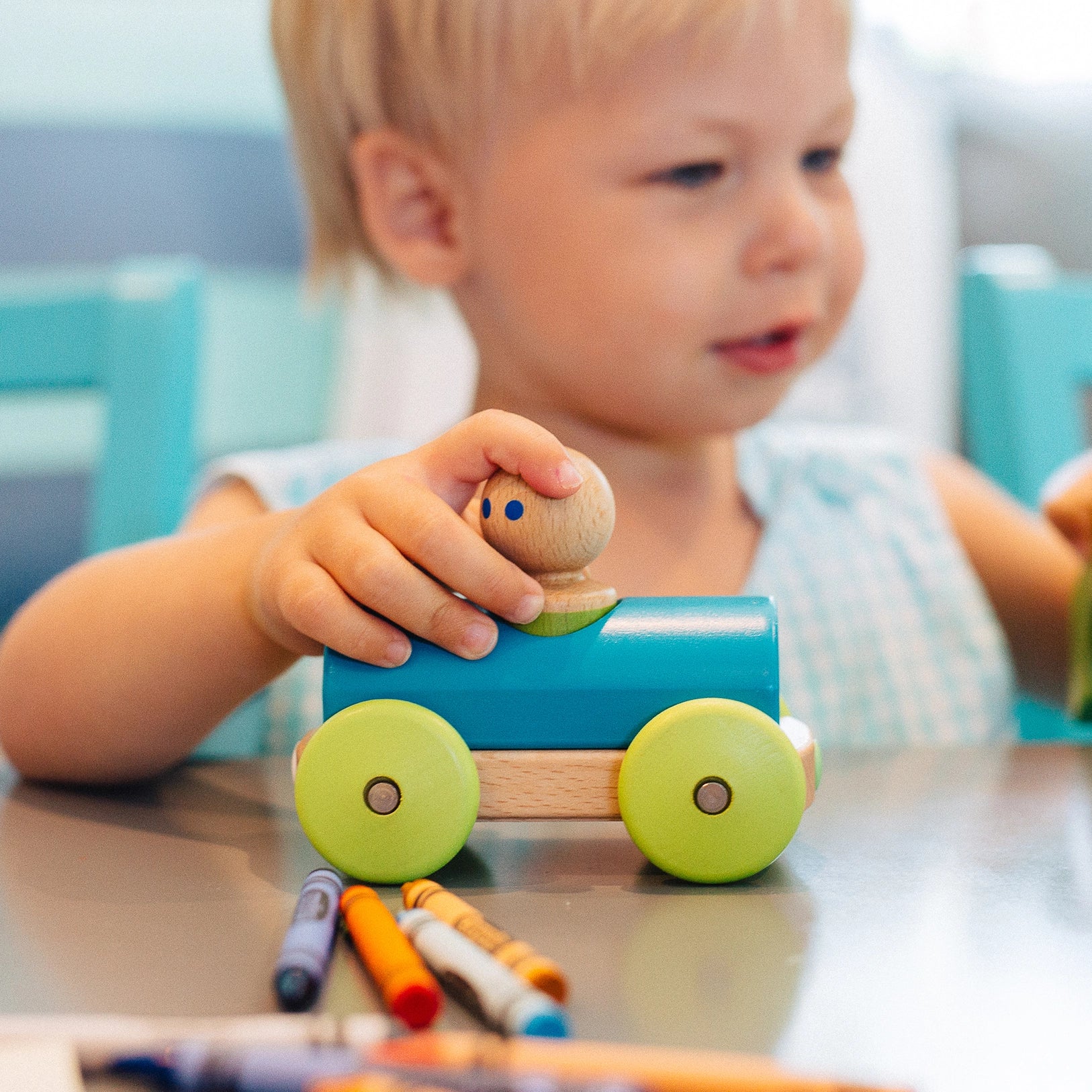 Child playing with a wooden toy car on a table