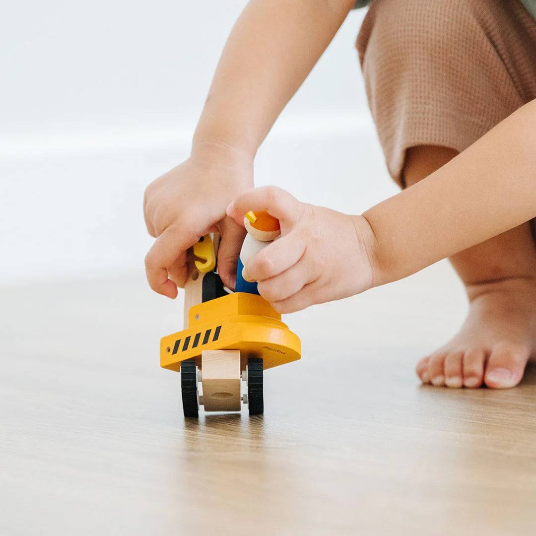 Child playing with a yellow toy on a light wooden floor.