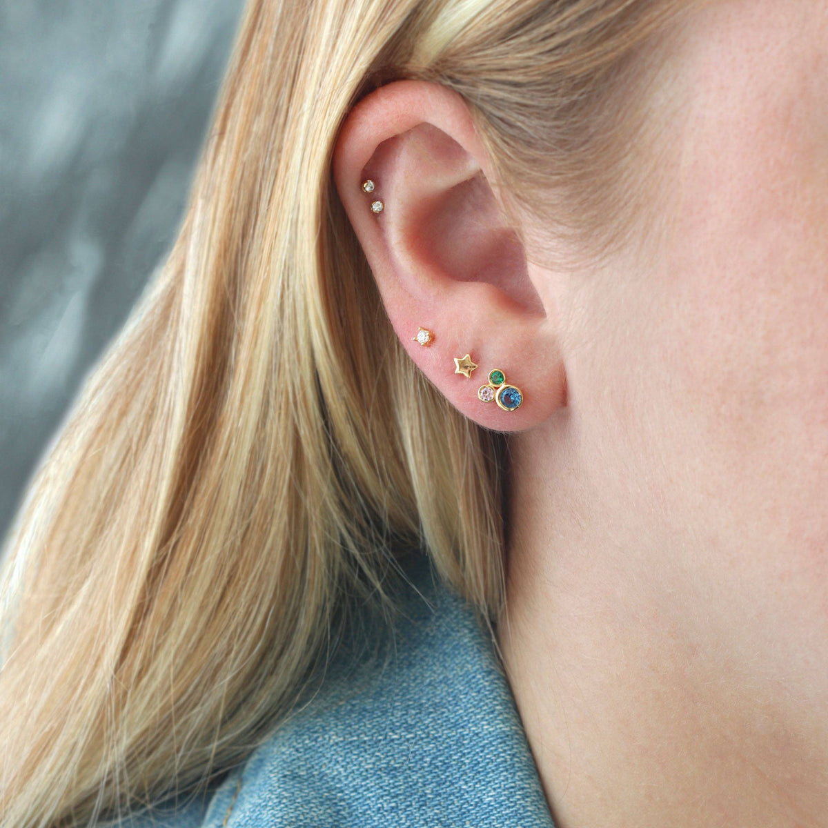 Close-up of an ear with multiple earrings against a neutral background