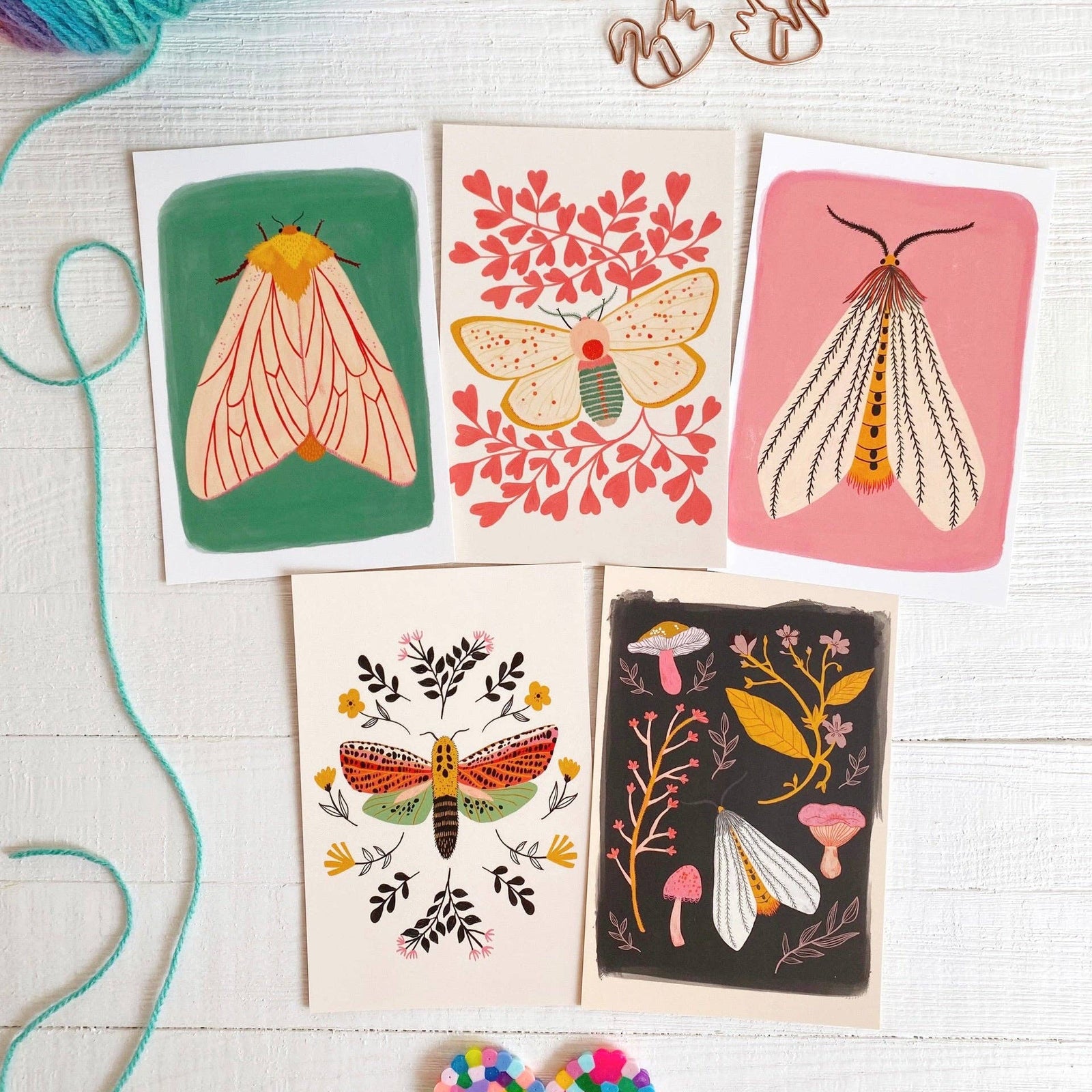 Colorful moths on postcards with decorative elements on a light wooden surface.