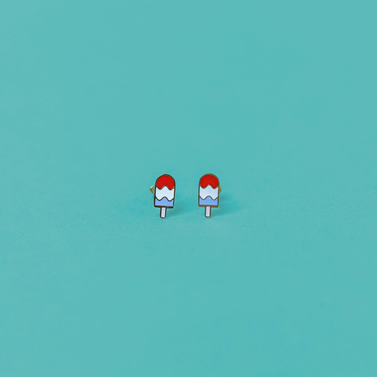 Small red and white popsicle-shaped earrings on a teal background