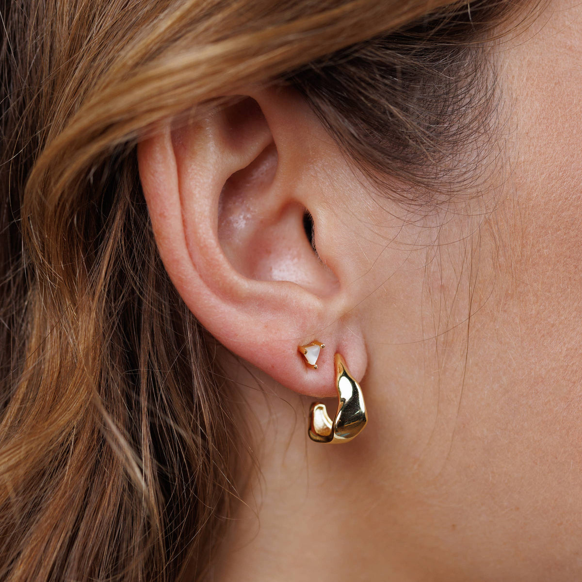 Close-up of a person wearing gold earrings with a blurred background