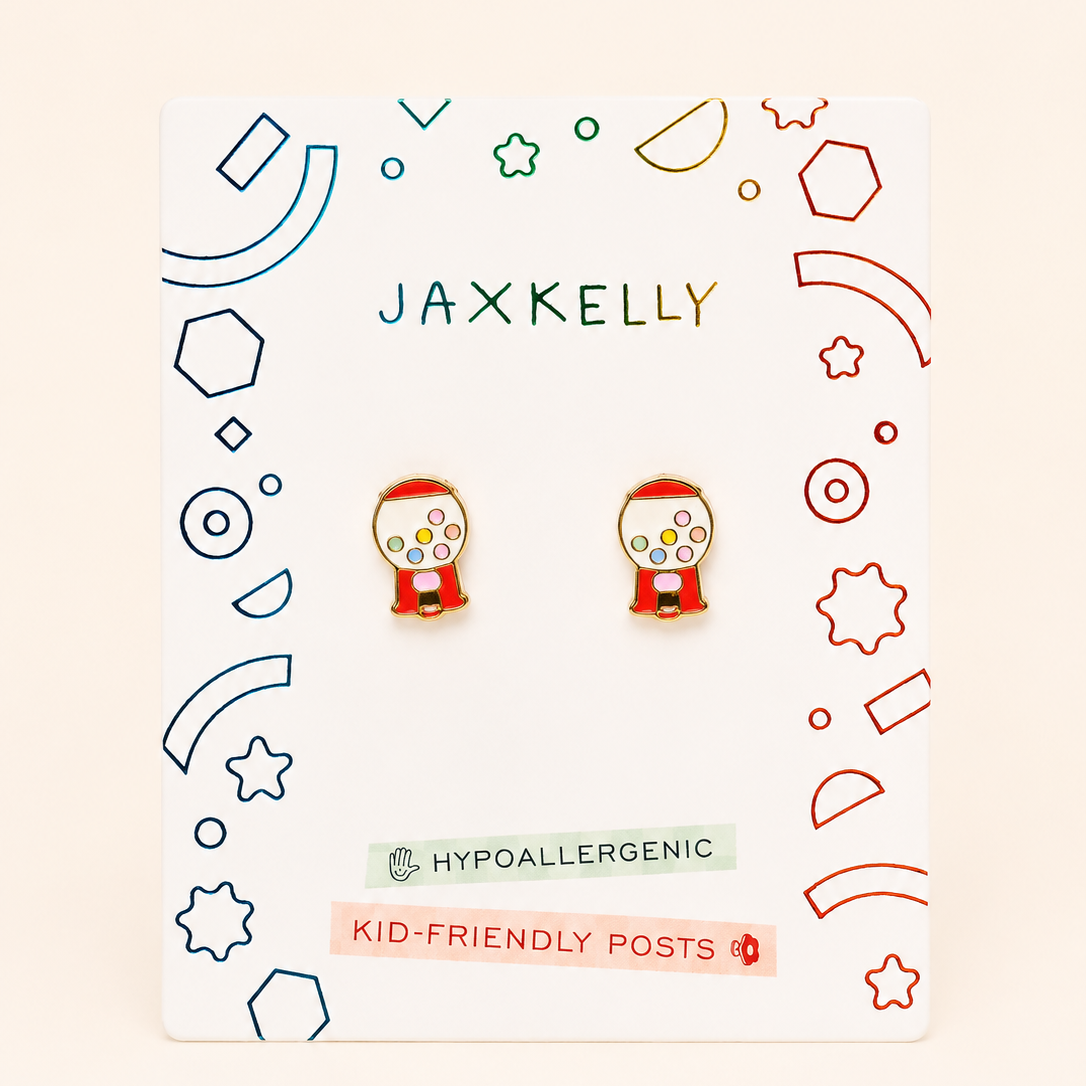 A pair of small gumball machine stud earrings displayed on a branded white backing card. The earrings are red with yellow and white details, and the card reads JAXKELLY, HYPOALLERGENIC, and KID-FRIENDLY POSTS.