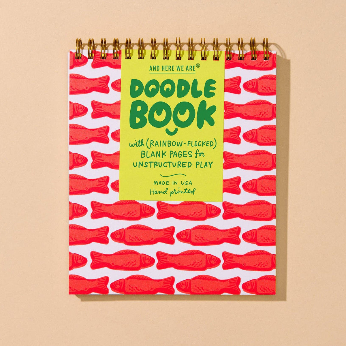 A spiral-bound children's activity book titled 'Doodle Book' with a bright yellow front cover, red fish illustrations, and gold wire binding, shown against a warm beige background.