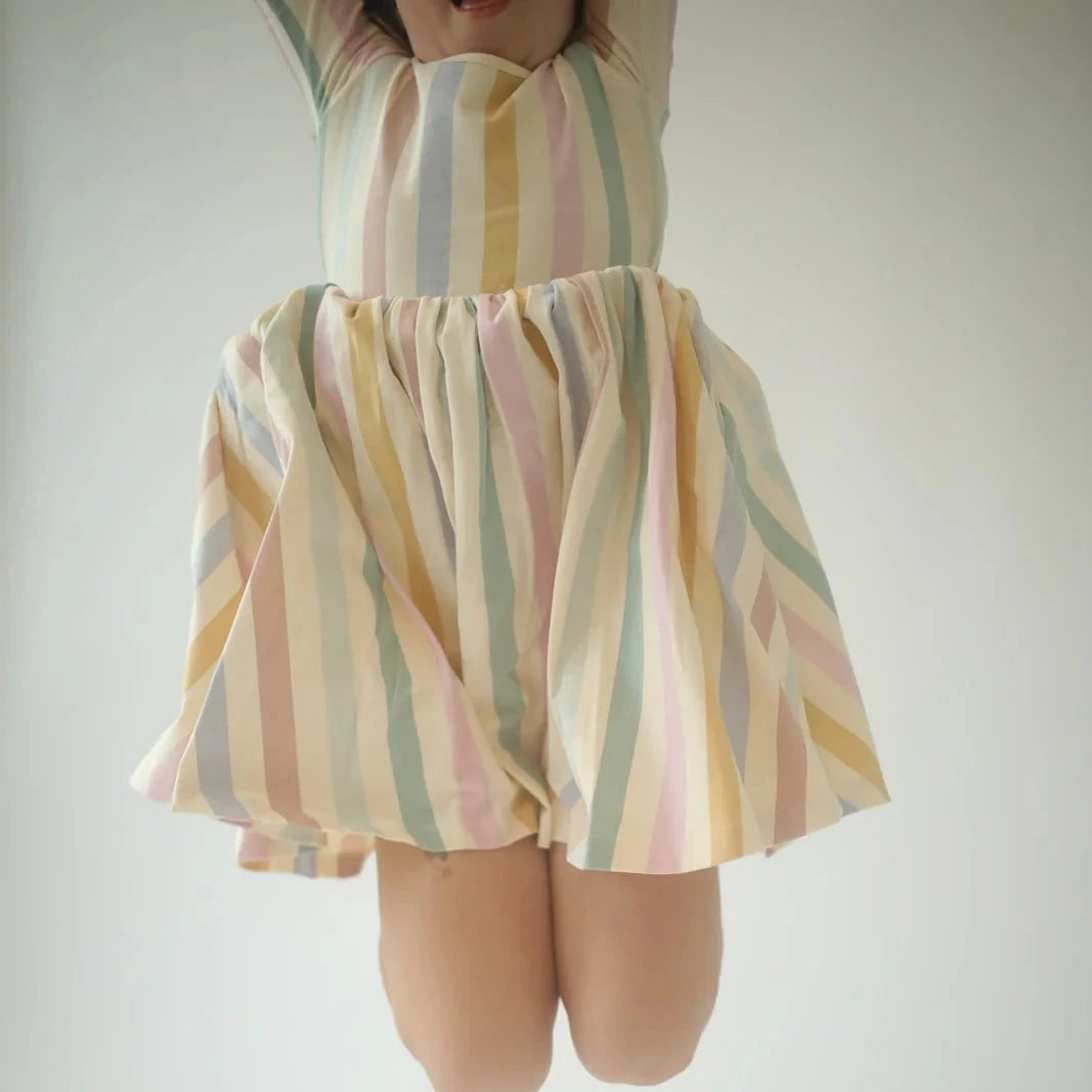 Child jumping in s Pastel striped dress on a plain background