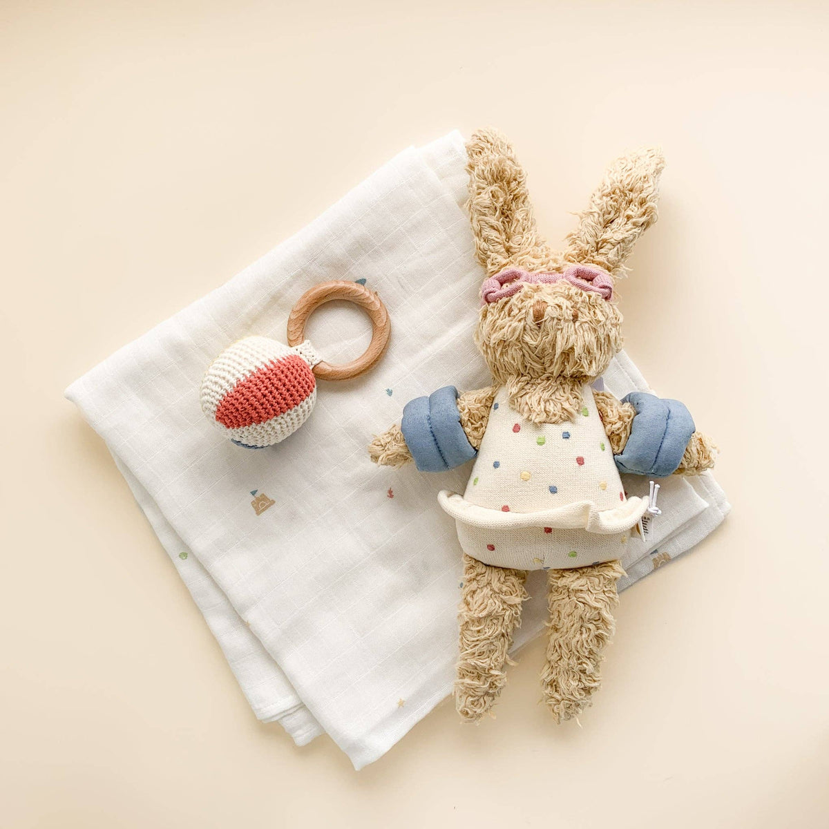 Stuffed bunny toy with a wooden ring and knitted ball on a white blanket against a beige background