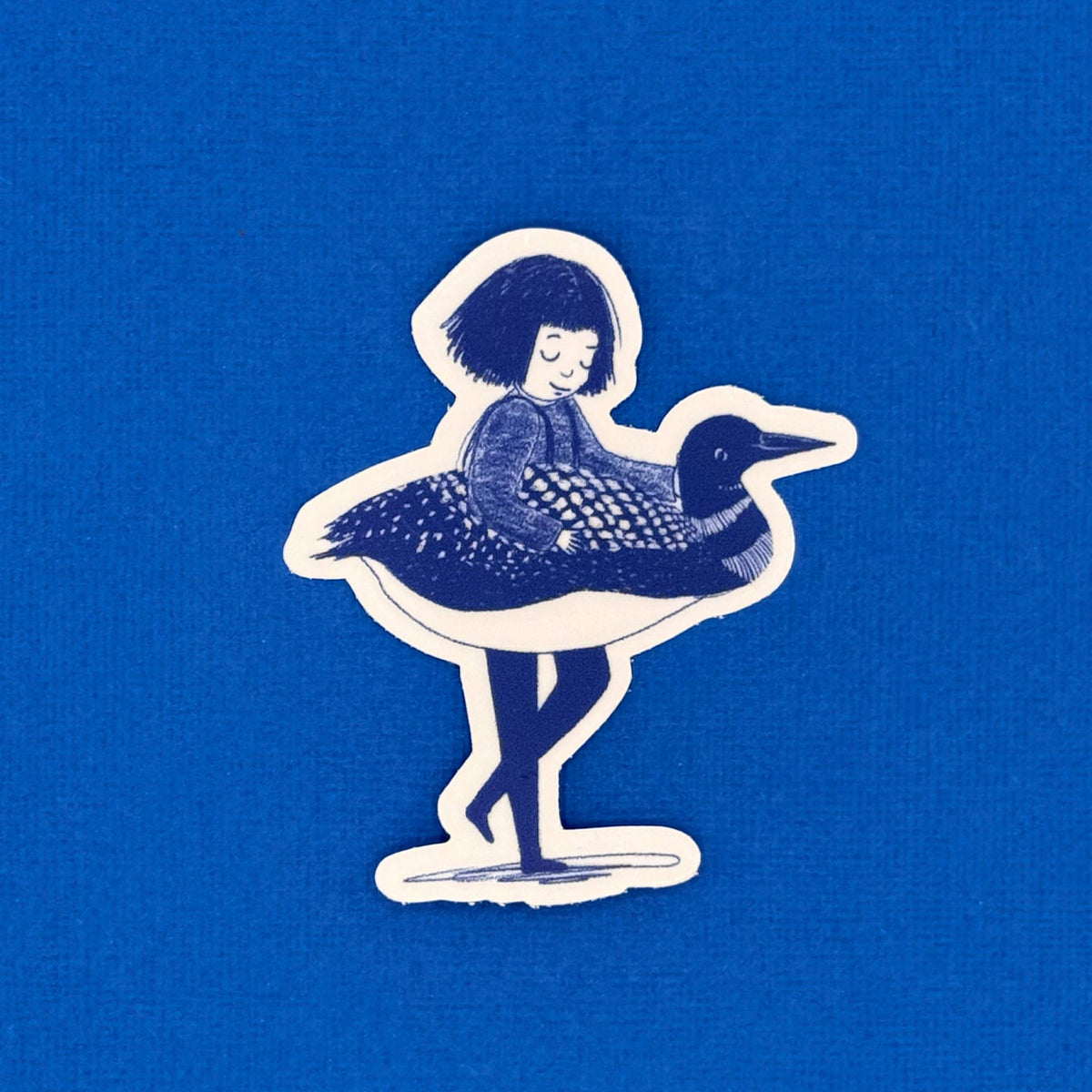 A die-cut sticker featuring an illustration of a woman riding a loon, shown on a solid blue textured background.