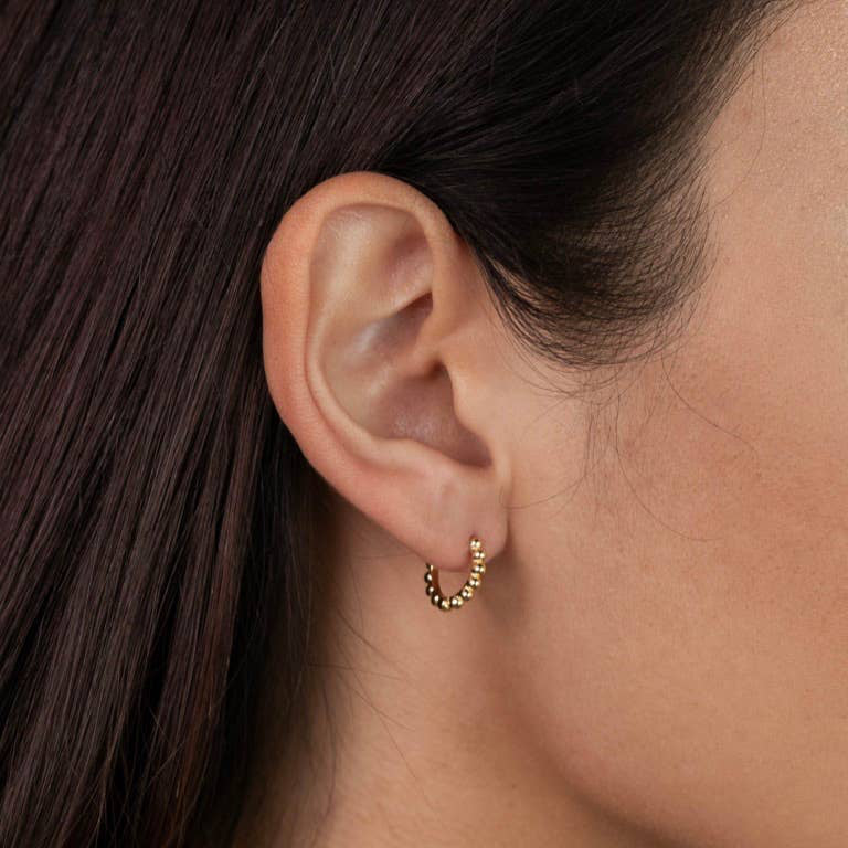 A pair of small gold-colored ball hoop earrings with curved ear wires and snap closures on a plain background.
