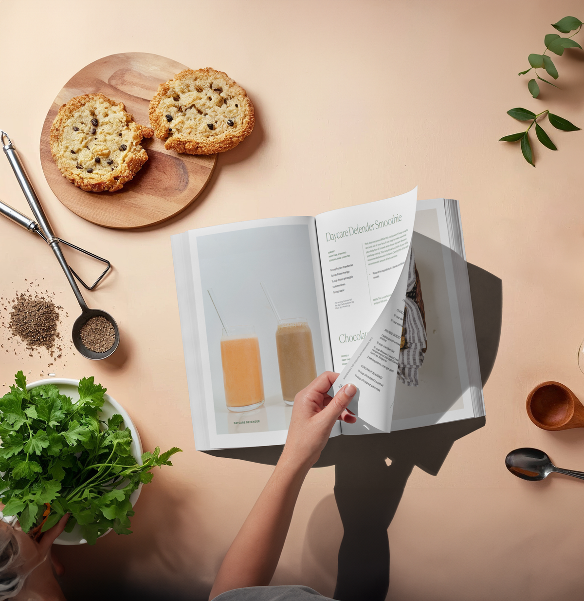 Open cookbook on a table with food items and a hand holding the book