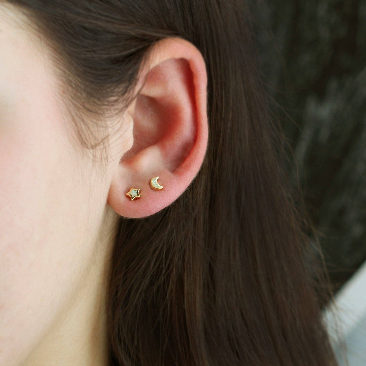 Close-up of an ear wearing gold star and moon earrings with blurred background